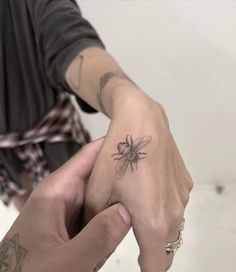 two hands holding each other with tattoos on their fingers and one has a bee tattoo on it