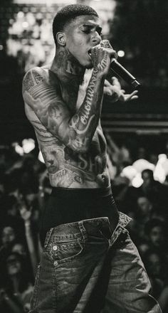 a man with tattoos on his arm and chest holding a microphone in front of him