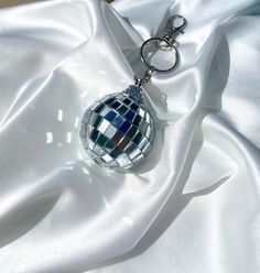 a disco ball keychain sitting on top of a white satin material covered surface