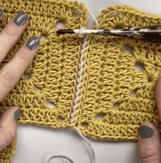 two hands are crocheting together on a piece of yellow fabric with white yarn