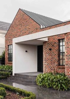 a brick house with a black door and some plants in front of the entryway