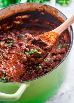 a wooden spoon in a green pot filled with meatballs and tomato sauce on a marble surface