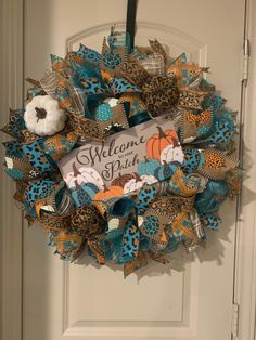 a welcome fall wreath hanging on the front door with an orange and blue pumpkin decoration