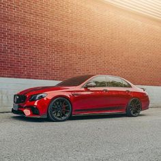 a red mercedes s - class parked in front of a brick wall with black rims