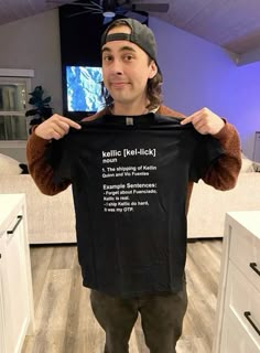 a man holding up a black t - shirt with words on it in front of his face