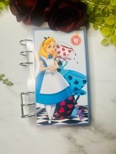 a notepad with an image of alice in wonderland on it next to some flowers