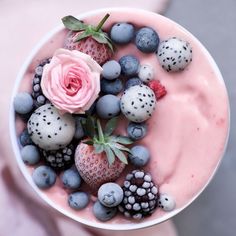 a white bowl filled with berries and blueberries next to a pink rose on top