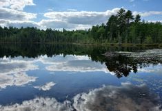 the sky is reflected in the still water of a lake surrounded by trees and clouds