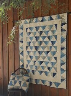 a chair sitting next to a quilt hanging on a wooden wall with a tree in the background