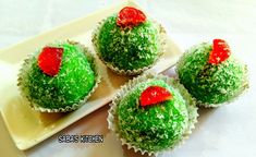 four cupcakes with green frosting and red sprinkles on top