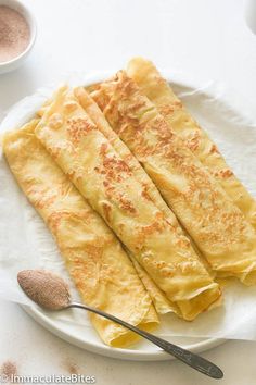 three pieces of crepe on a white plate with a spoon next to it