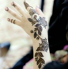 a woman's hand with henna tattoos on her left arm and hands, both decorated with flowers