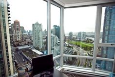 a desk with a laptop on top of it in front of large windows overlooking the city