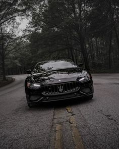 a black masera is parked on the side of the road in front of some trees