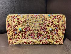 Beautiful hand-embroidered floral silk clutch bag inlaid with semi-precious stones. The front is completely covered in the design and has a closure flap with magnettic snap fastening. This clutch is perfect for daytime or night time. It is the ideal size for fitting all your essentials. It is a stylish accessory for each & every occasion. This equisite piece is even ideal for gifting to your near & dear one's . Thread - Silk Fabric - Velvet Variety of Semi-precious stones are used in this piece Zardozi is a type of heavy and elaborate metal embroidery on silk, satin, or velvet fabric base. Designs are often created using gold and silver wires and can incorporate pearls, beads, and precious stones. The embroidered silk clutch bag is made in Agra, India & is fully handmade. Designed to compl Traditional Red Embroidered Evening Bag, Rectangular Clutch With Gold Embroidery For Festivals, Rectangular Gold Embroidered Clutch For Festivals, Rectangular Gold Embroidery Clutch For Festivals, Luxury Clutch With Gold Embroidery For Festivals, Luxury Embroidered Evening Bag For Festive Occasions, Traditional Embellished Rectangular Evening Bag, Traditional Red Embellished Clutch, Gold Clutch With Intricate Embroidery For Festivals