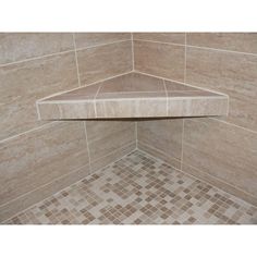 the corner of a shower stall with tiled flooring and walls in beige tones,