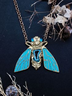 a blue and gold necklace with a large bee on it's back, surrounded by branches