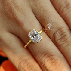 a woman's hand with a diamond ring on top of her finger and an orange object in the background