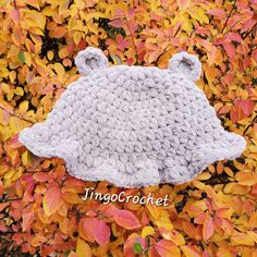 a crocheted bear hat hanging from a tree with autumn leaves in the background