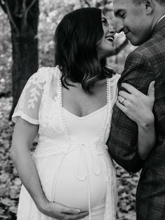 a pregnant couple cuddles in the woods while holding each other's belly