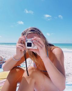 a woman sitting on the beach taking a photo with her camera