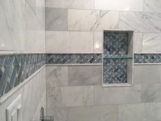 a bathroom with white marble and blue glass tiles on the shower wall, along with an open shelf