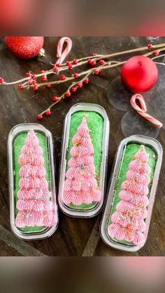 three tins filled with green and pink frosted christmas trees on top of a wooden table