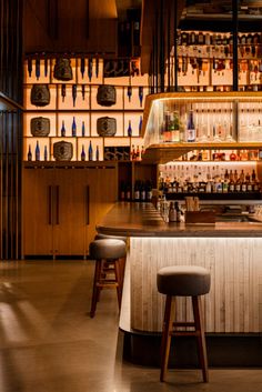 a bar with stools in front of it and shelves full of bottles on the wall