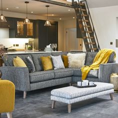 a living room with grey couches and yellow pillows on the chair, next to a stair case