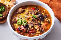 a white bowl filled with mexican soup next to a wooden spoon and some green peppers