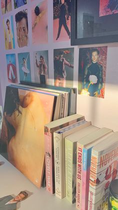 several books are stacked on top of each other in front of a wall covered with pictures