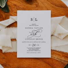 the wedding stationery is laid out on a wooden platter with white napkins and greenery