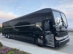 a black tour bus parked on the side of the road next to some purple flowers