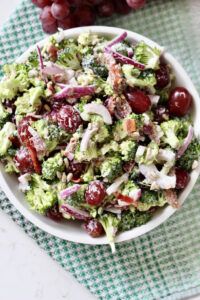 a white bowl filled with broccoli salad next to grapes