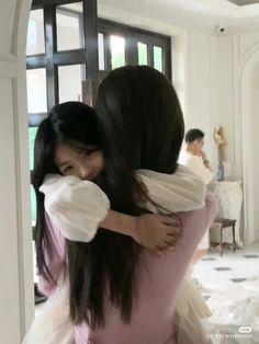 two women hugging each other in front of a doorway with people standing around the room behind them