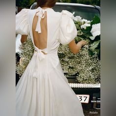 the back of a woman's wedding dress, with flowers in the car behind her