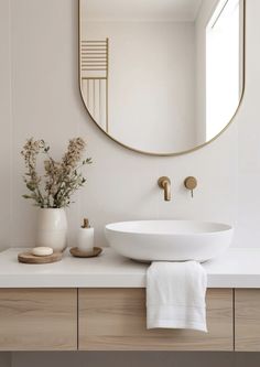 a white sink sitting under a round mirror next to a vase with flowers in it