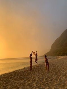 three people jumping up in the air on a beach at sunset with mountains in the background