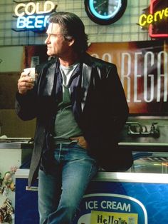 a man sitting on top of a ice cream stand holding a cup in his hand