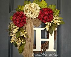 a wreath with red and white flowers is hanging on a front door, next to the letter h