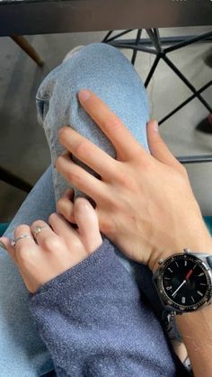 a person with their hand on the wrist of another person wearing a watch and sitting down