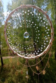 a dream catcher hanging from the side of a tree in front of some green trees