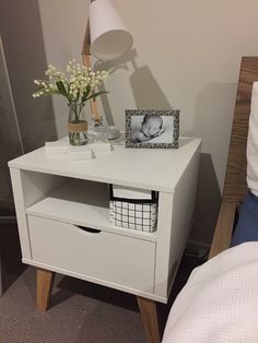 a small white nightstand with flowers on it next to a night stand and a lamp