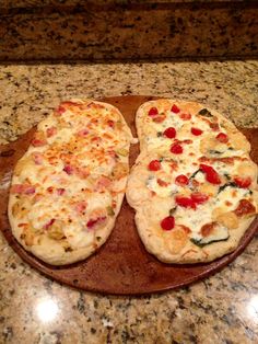 two pizzas sitting on top of a wooden platter covered in cheese and toppings