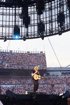 a man standing on top of a stage holding a guitar in front of an audience