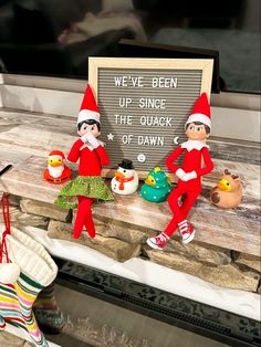 there are two elfs sitting on the mantle next to a sign that says we've been up since the quack of dawn