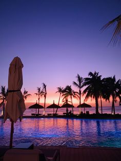 the sun is setting over an empty swimming pool with umbrellas and palm trees in the foreground