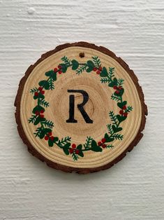 a wood slice with the letter r painted on it and holly wreaths around it