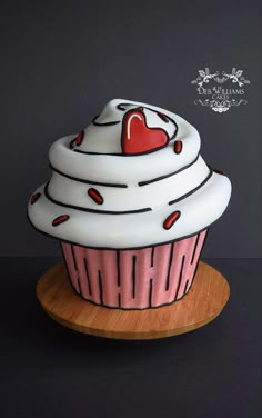 a cupcake with a heart on top sitting on a wooden plate in front of a black background