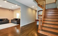 a living room filled with furniture next to a wooden stair case on top of a hard wood floor